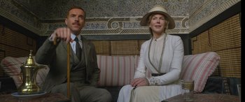 Movie still from “Queen of the Desert” (2015), directed by Werner Herzog – A man and a woman sitting on a couch in a room; Medium shot, Low angle