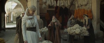 Movie still from “Queen of the Desert” (2015), directed by Werner Herzog – A man and a woman standing next to each other in a market; Medium shot, Over the shoulder angle
