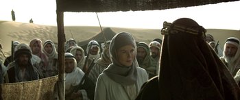 Movie still from “Queen of the Desert” (2015), directed by Werner Herzog – A group of people standing in a field; Medium shot, Over the shoulder angle