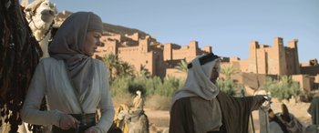 Movie still from “Queen of the Desert” (2015), directed by Werner Herzog – Two men in traditional clothing standing next to each other in front of a building; Medium shot, Low angle