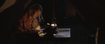 Movie still from “Queen of the Desert” (2015), directed by Werner Herzog – A woman sitting at a table with a book and a lamp; Medium shot, Low angle