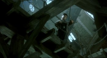 Movie still from “Quills” (2000), directed by Philip Kaufman – A man in chains climbing up a wooden structure; Wide shot, Low angle