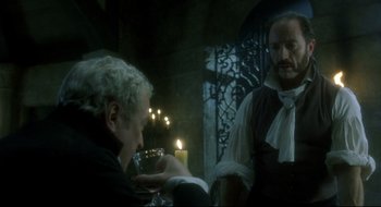 Movie still from “Quills” (2000), directed by Philip Kaufman – Two men in medieval garb sitting at a dinner table; Medium shot, Over the shoulder angle