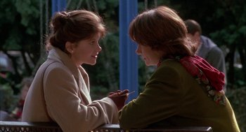 Movie still from “Raising Cain” (1992), directed by Brian De Palma – Two women sitting on a bench one holding a cell phone; Medium shot, Over the shoulder angle