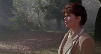 Movie still from “Raising Cain” (1992), directed by Brian De Palma – A woman in a tan coat standing in a forest; Medium shot, Over the shoulder angle