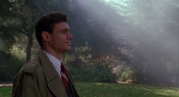 Movie still from “Raising Cain” (1992), directed by Brian De Palma – A man in a suit and tie standing in front of a forest; Close Up shot, Low angle