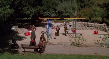 Movie still from “Raising Cain” (1992), directed by Brian De Palma – A group of people standing on a playground; Extreme Wide shot, High angle