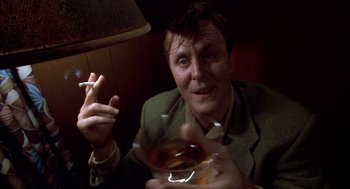 Movie still from “Raising Cain” (1992), directed by Brian De Palma – A man sitting at a table with a glass of whiskey; Close Up shot, Low angle
