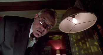 Movie still from “Raising Cain” (1992), directed by Brian De Palma – A man in a suit and tie standing in front of a lamp; Close Up shot, Low angle