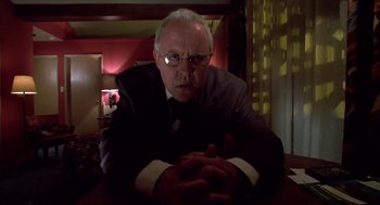 Movie still from “Raising Cain” (1992), directed by Brian De Palma – An older man sitting at a table with his hands crossed; Close Up shot, Low angle
