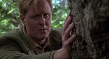 Movie still from “Raising Cain” (1992), directed by Brian De Palma – A man leaning against a tree looking at the camera; Close Up shot, Over the shoulder angle