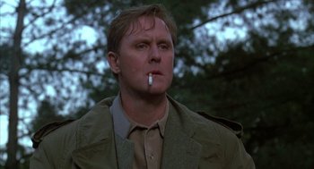 Movie still from “Raising Cain” (1992), directed by Brian De Palma – A man smoking a cigarette while standing in the woods; Close Up shot, Low angle