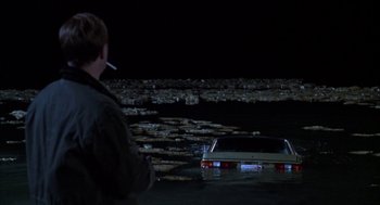 Movie still from “Raising Cain” (1992), directed by Brian De Palma – A man standing next to a car in the middle of a body of water at night; Wide shot, High angle