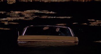 Movie still from “Raising Cain” (1992), directed by Brian De Palma – A man waving from the back of a car in the dark; Extreme Wide shot, High angle