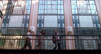 Movie still from “Raising Cain” (1992), directed by Brian De Palma – A group of people walking in front of a glass building; Extreme Wide shot, Low angle