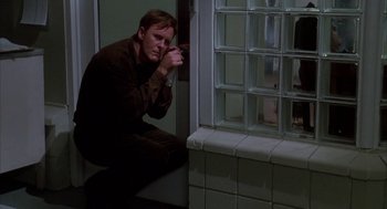 Movie still from “Raising Cain” (1992), directed by Brian De Palma – A man leaning against a wall looking out a window; Medium shot, High angle
