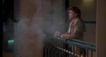 Movie still from “Raising Cain” (1992), directed by Brian De Palma – A woman is smoking a cigarette on a balcony railing; Wide shot, Low angle