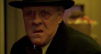 Movie still from “Raising Cain” (1992), directed by Brian De Palma – An older man wearing a hat and glasses; Close Up shot, Low angle