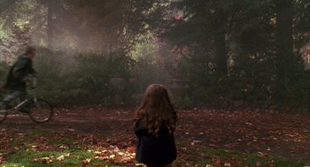 Movie still from “Raising Cain” (1992), directed by Brian De Palma – A young girl sitting on the ground in the woods; Wide shot, Over the shoulder angle