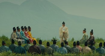 Movie still from “Ran” (1985), directed by Akira Kurosawa – A group of people sitting in a field with a priest; Extreme Wide shot, Low angle