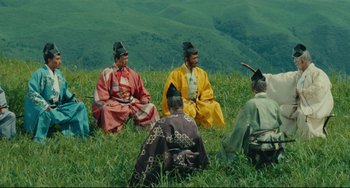 Movie still from “Ran” (1985), directed by Akira Kurosawa – A group of people sitting in a field wearing traditional clothing; Wide shot, High angle