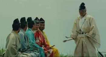 Movie still from “Ran” (1985), directed by Akira Kurosawa – A group of men sitting next to each other on a field; Wide shot, Over the shoulder angle