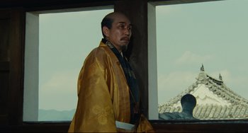 Movie still from “Ran” (1985), directed by Akira Kurosawa – A man in a yellow robe standing in front of a window; Medium shot, Low angle