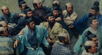 Movie still from “Ran” (1985), directed by Akira Kurosawa – A group of men sitting next to each other on the ground; Wide shot, High angle