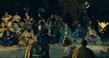 Movie still from “Ran” (1985), directed by Akira Kurosawa – A group of people sitting on the ground in front of a tree; Wide shot, High angle
