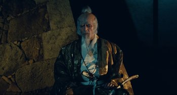 Movie still from “Ran” (1985), directed by Akira Kurosawa – An old man with a long white beard sitting in a chair; Medium shot, Low angle