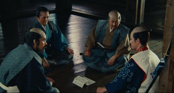 Movie still from “Ran” (1985), directed by Akira Kurosawa – A group of men sitting on the ground in a circle; Wide shot, High angle