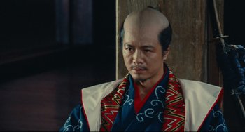 Movie still from “Ran” (1985), directed by Akira Kurosawa – A man with a bald head is wearing a kimono; Close Up shot, High angle