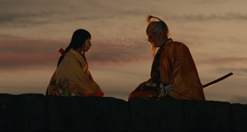 Movie still from “Ran” (1985), directed by Akira Kurosawa – A man and a woman sitting next to each other on top of a hill; Medium shot, Low angle