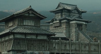 Movie still from “Ran” (1985), directed by Akira Kurosawa – A building with a fence and a wooden fence; Extreme Wide shot, Low angle