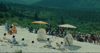 Movie still from “Ran” (1985), directed by Akira Kurosawa – A group of people sitting on top of a hill under umbrellas; Extreme Wide shot, High angle