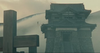 Movie still from “Ran” (1985), directed by Akira Kurosawa – A fire hydrant spewing water into the air near a building; Extreme Wide shot, Low angle