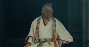 Movie still from “Ran” (1985), directed by Akira Kurosawa – An old man dressed in a white kimono; Medium shot, Low angle