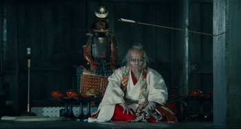 Movie still from “Ran” (1985), directed by Akira Kurosawa – An old man wearing a kimono sitting in front of a samurai; Wide shot, Low angle