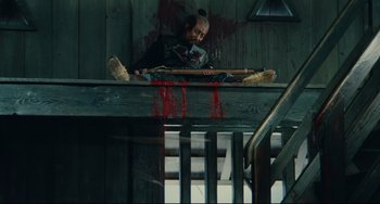 Movie still from “Ran” (1985), directed by Akira Kurosawa – A man sitting on top of a wooden railing next to stairs; Wide shot, Overhead angle