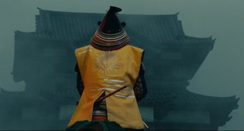 Movie still from “Ran” (1985), directed by Akira Kurosawa – A person wearing a hat and a yellow vest; Medium shot, Low angle