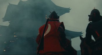 Movie still from “Ran” (1985), directed by Akira Kurosawa – A person wearing a red and black uniform and a red helmet; Wide shot, Low angle
