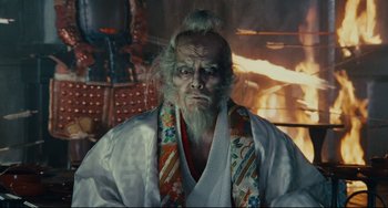 Movie still from “Ran” (1985), directed by Akira Kurosawa – An old man with long white hair wearing a white robe; Close Up shot, Low angle
