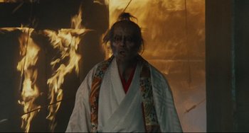 Movie still from “Ran” (1985), directed by Akira Kurosawa – An old man wearing a white robe in front of a fire; Medium shot, Low angle