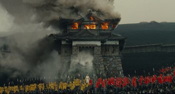 Movie still from “Ran” (1985), directed by Akira Kurosawa – A group of people standing next to each other near a fire; Extreme Wide shot, Low angle