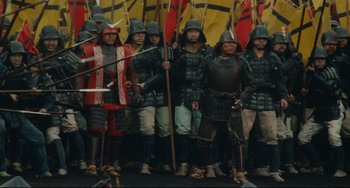 Movie still from “Ran” (1985), directed by Akira Kurosawa – A group of people in medieval costumes holding flags; Wide shot, High angle