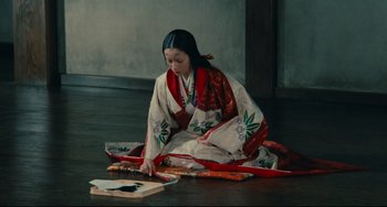 Movie still from “Ran” (1985), directed by Akira Kurosawa – A woman sitting on the ground wearing a red and white kimono; Medium shot, High angle