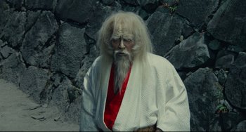 Movie still from “Ran” (1985), directed by Akira Kurosawa – An old man with long white hair and a white beard; Medium shot, Over the shoulder angle
