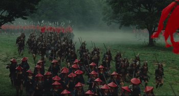 Movie still from “Ran” (1985), directed by Akira Kurosawa – A large group of people are marching through the field; Extreme Wide shot, High angle