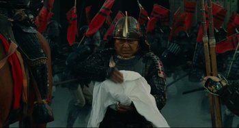 Movie still from “Ran” (1985), directed by Akira Kurosawa – A man in a samurai outfit holding a white cloth; Medium shot, Low angle