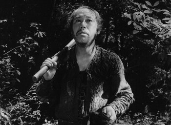 Movie still from “Rashomon” (1950), directed by Akira Kurosawa – A man holding a baseball bat while standing in the woods; Medium shot, Low angle